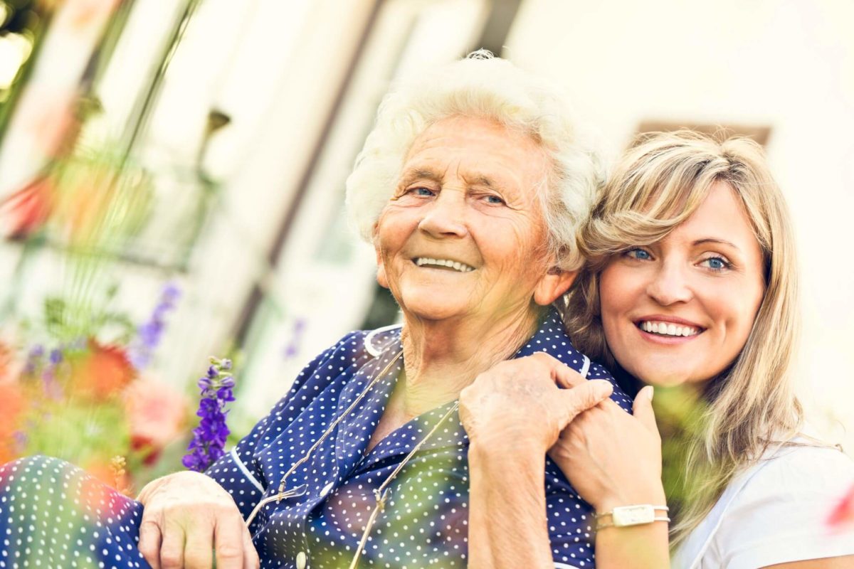 older adult with the adult child outside by flowers